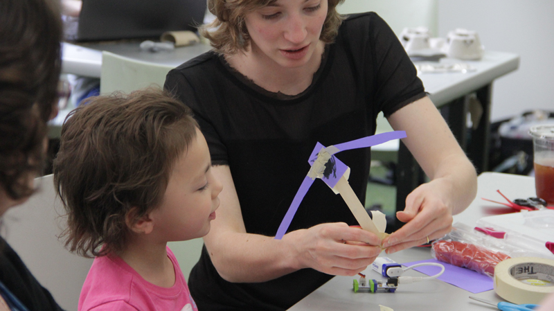 An artist-teacher assists a young participant at an ArtMakerSpace event.