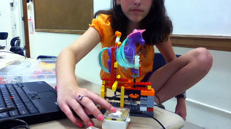 A student demonstrates an interactive kinetic sculpture incorporating found objects.
